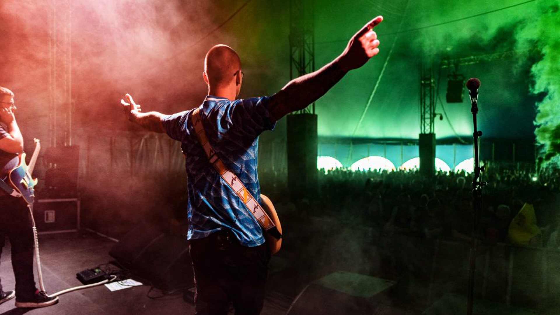 The Denabys frontman from behind, arms outstretched under red and green stage smoke to a festival crowd